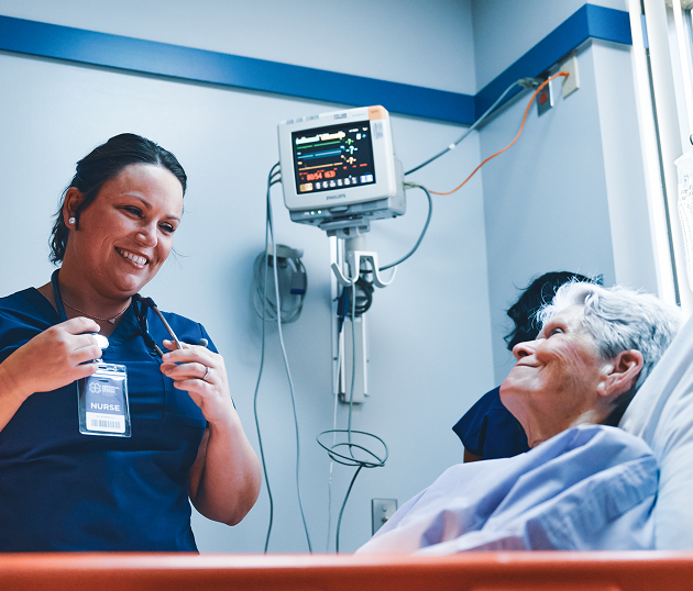 Female nurse smiling and talking to patient laying in hospital bed