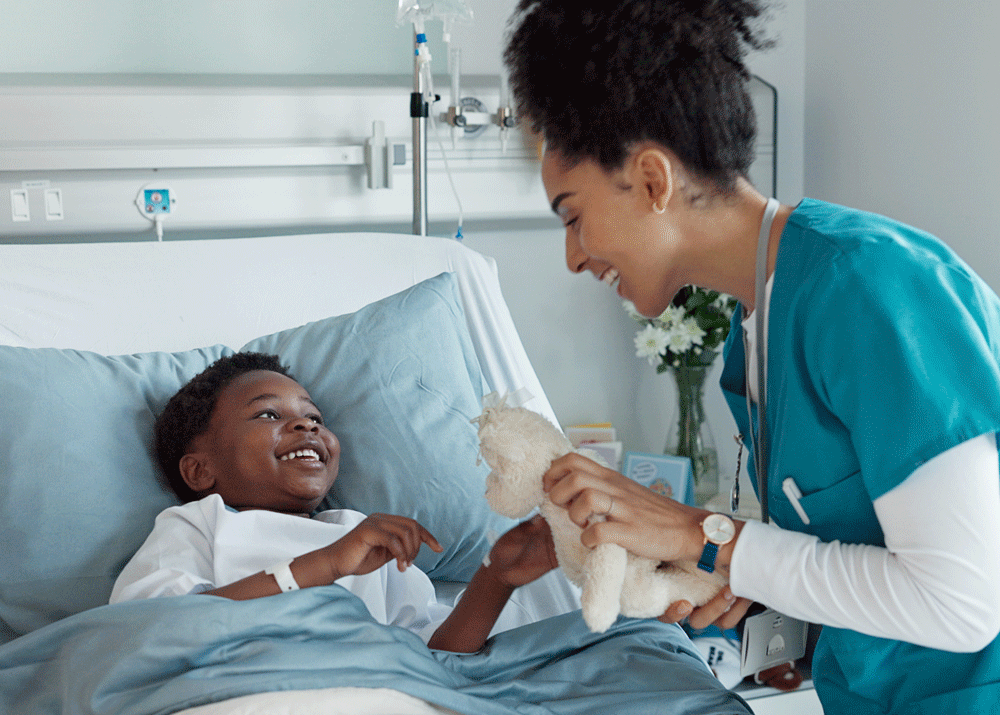 Nurse holding and playing with teddy bear while child smiles in bed