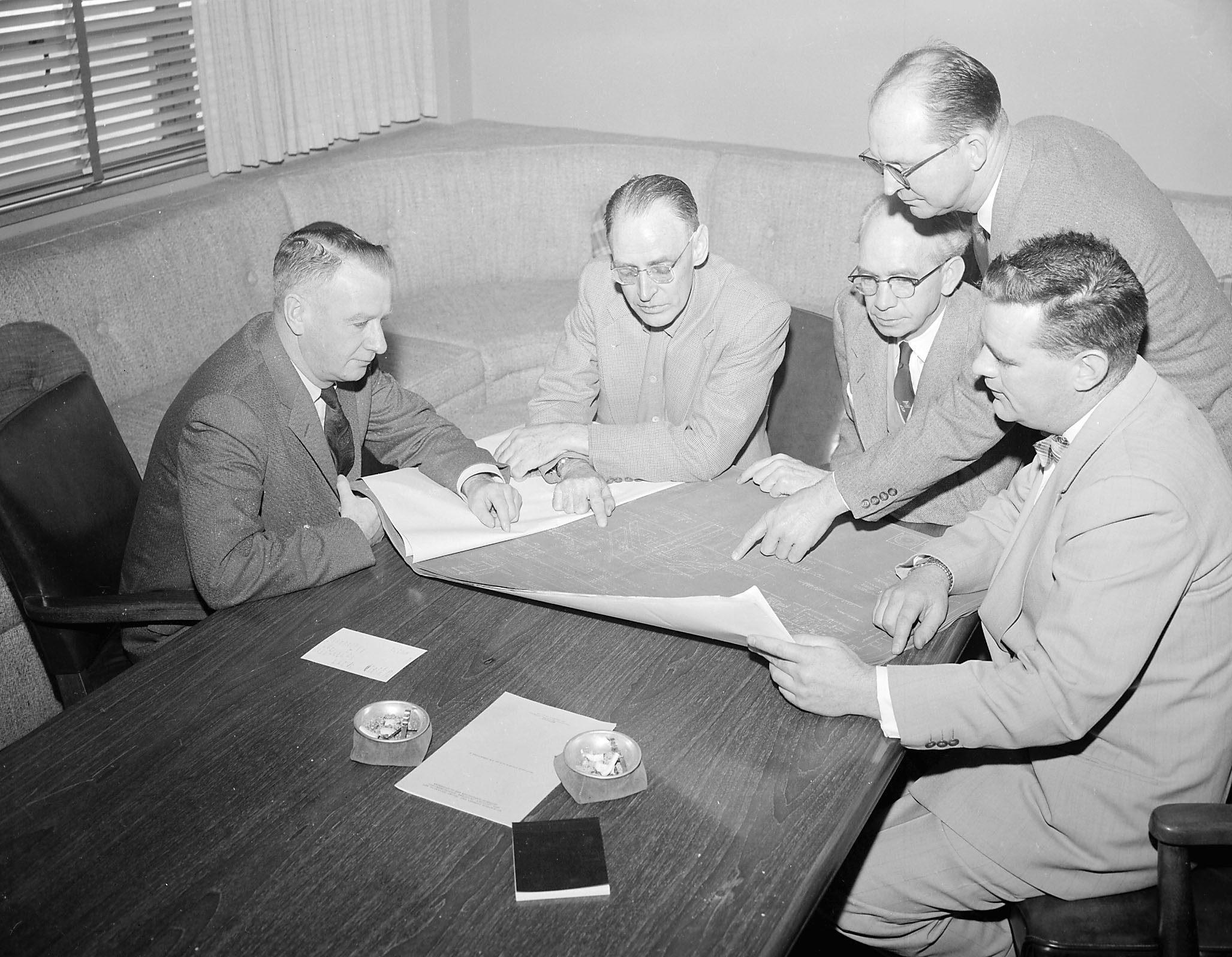Historical photograph of men looking over blueprints of hospital