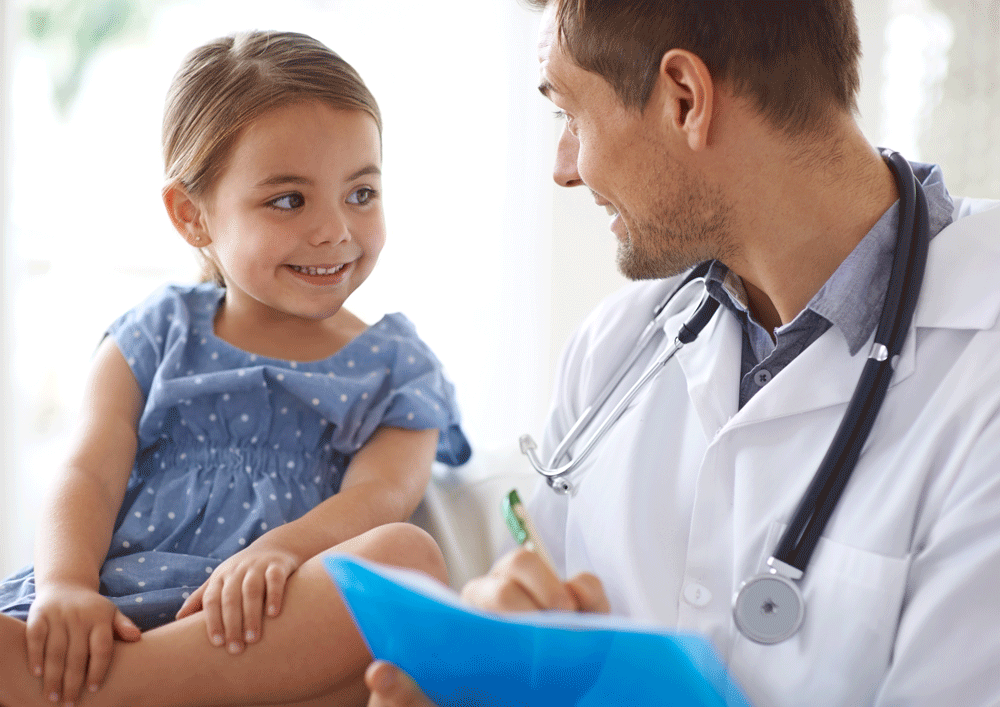 Little girl sitting on exam table smiling at pediatrician