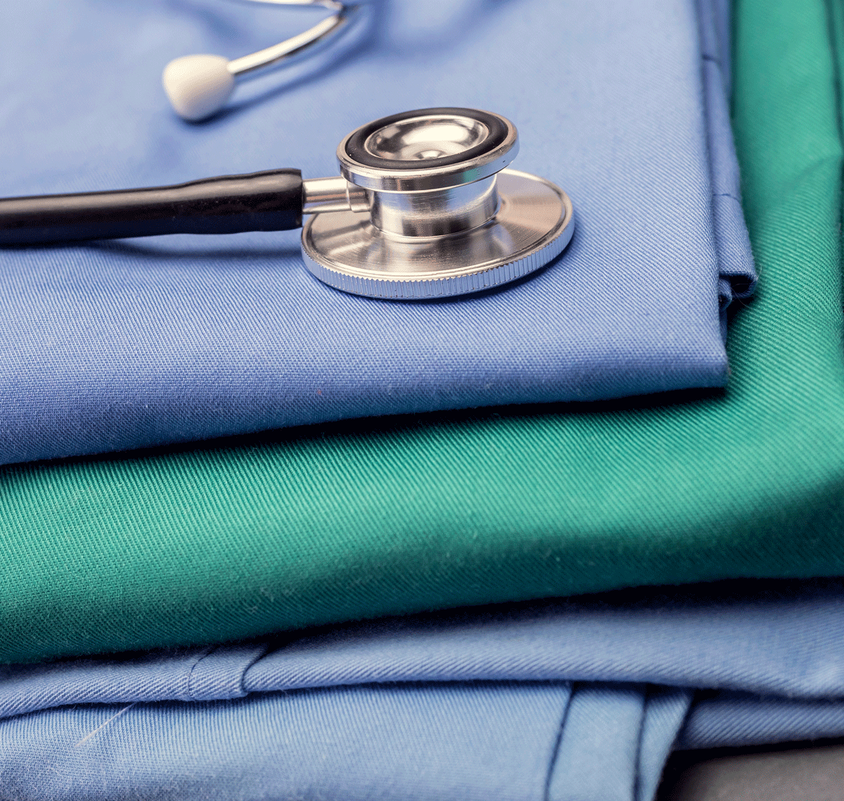 Stethoscope laying on pile of folded nursing scrubs